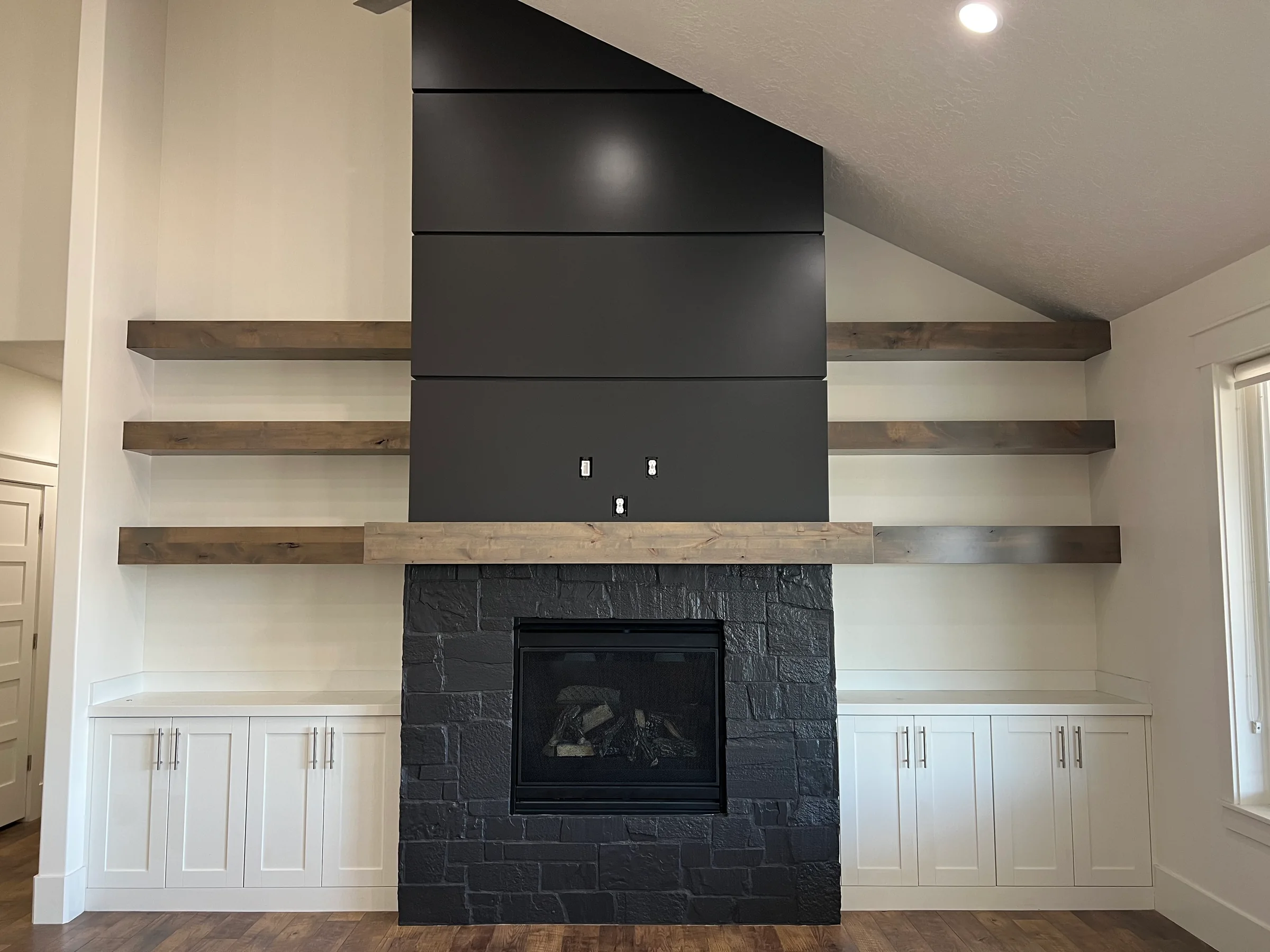 Dark fireplace feature wall with white built-in cabinetry and wood shelves.