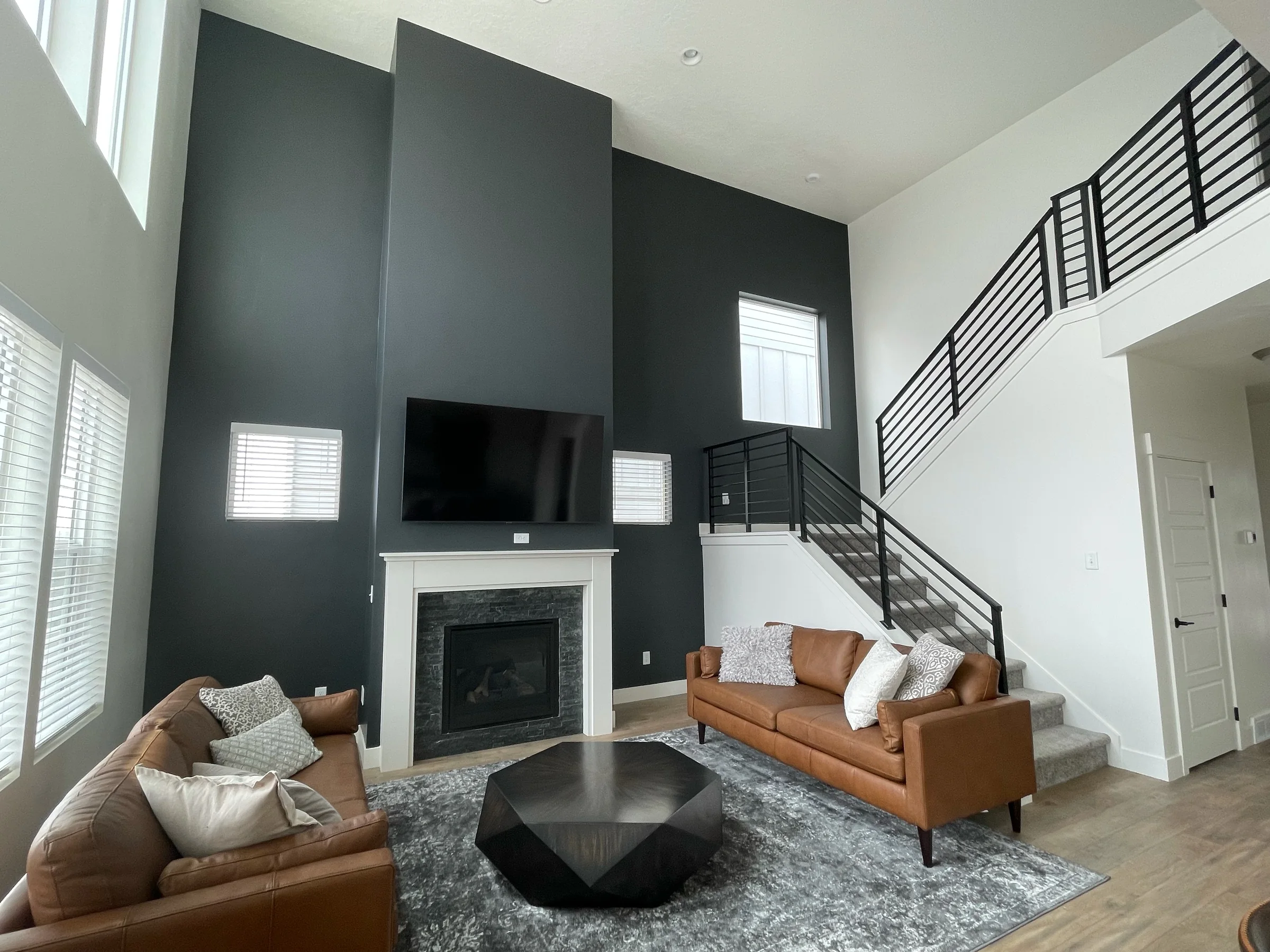 Tall living room with a dark fireplace wall, white walls and a staircase.