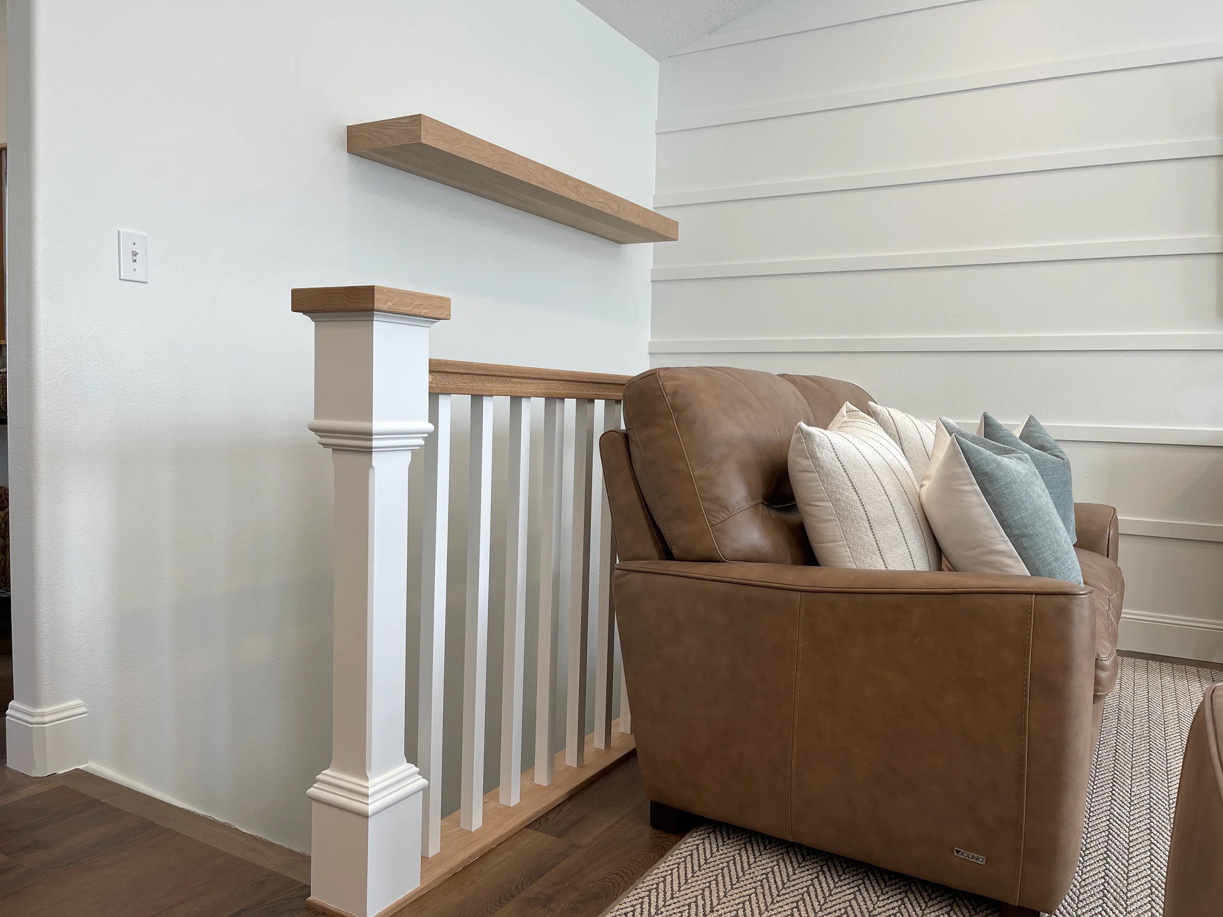 White wall paneling, stair trim and floating wood shelves beside a chair.