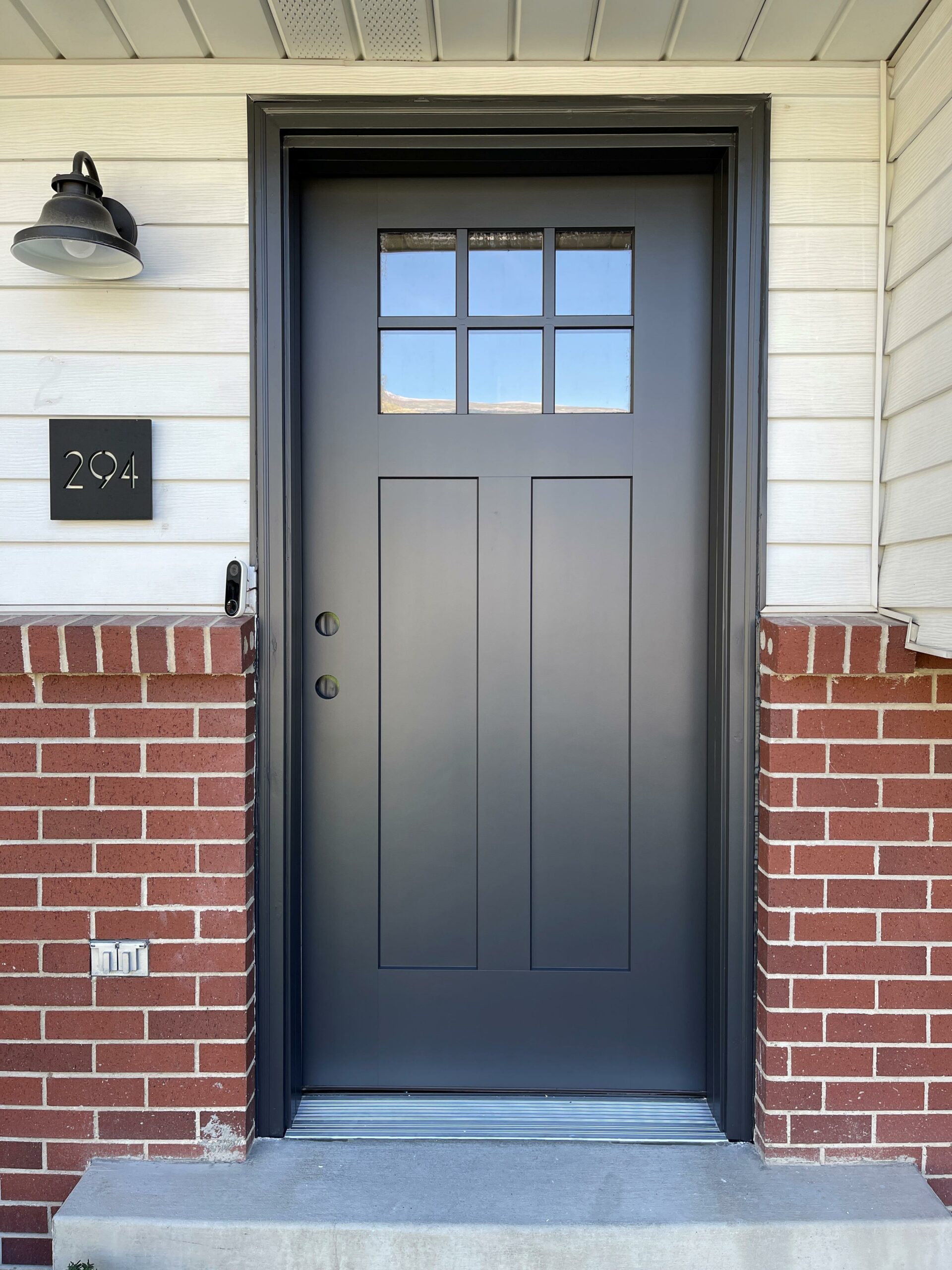 Dark front door beside white siding and brick
